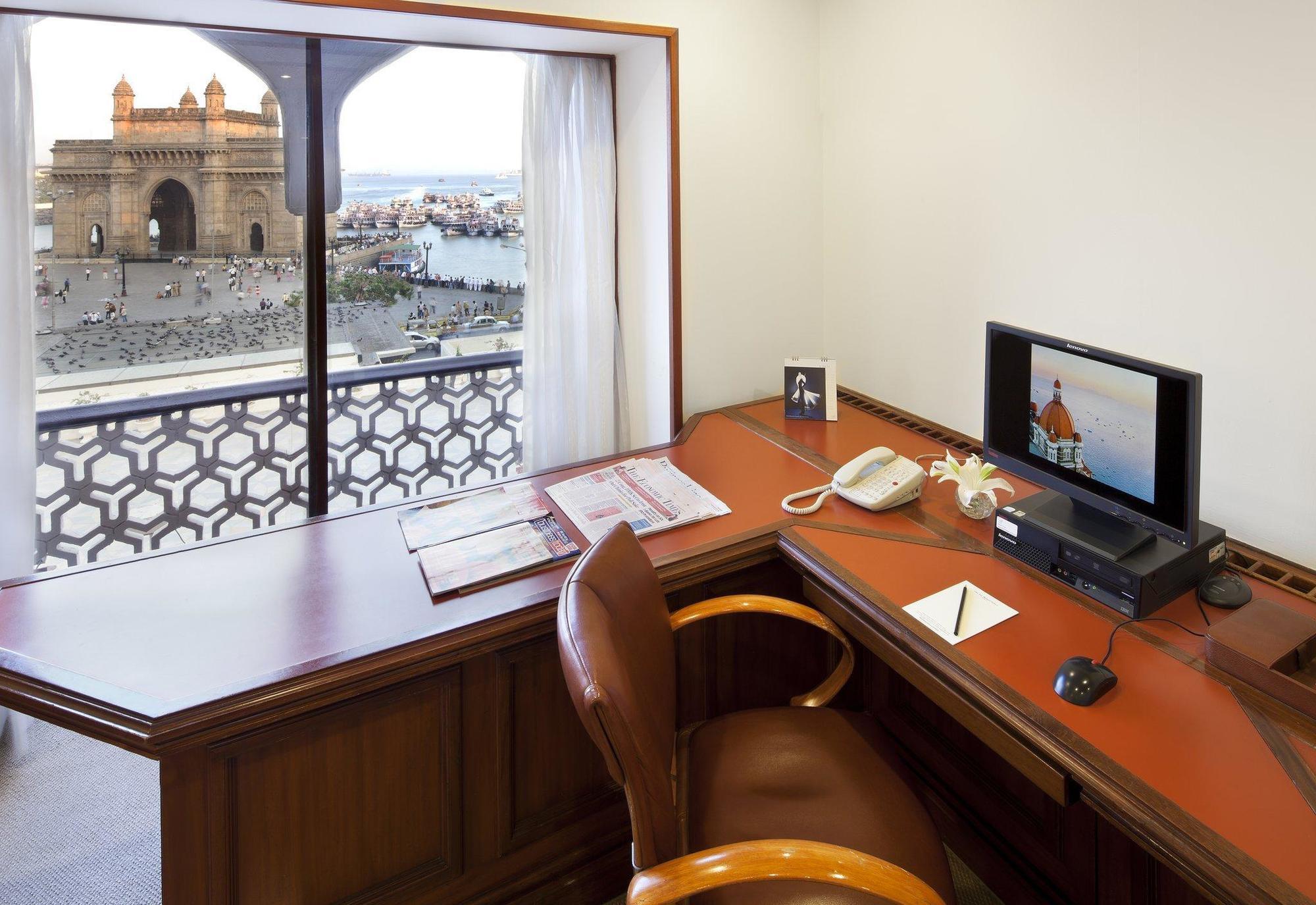 The Taj Mahal Tower, Mumbai Hotel Ngoại thất bức ảnh The photo shows a workspace with a wooden desk and an ergonomic chair. On the desk, there is a computer monitor, a telephone, and some stationery items. A window provides a view of an outdoor scene, possibly featuring water and structures or building